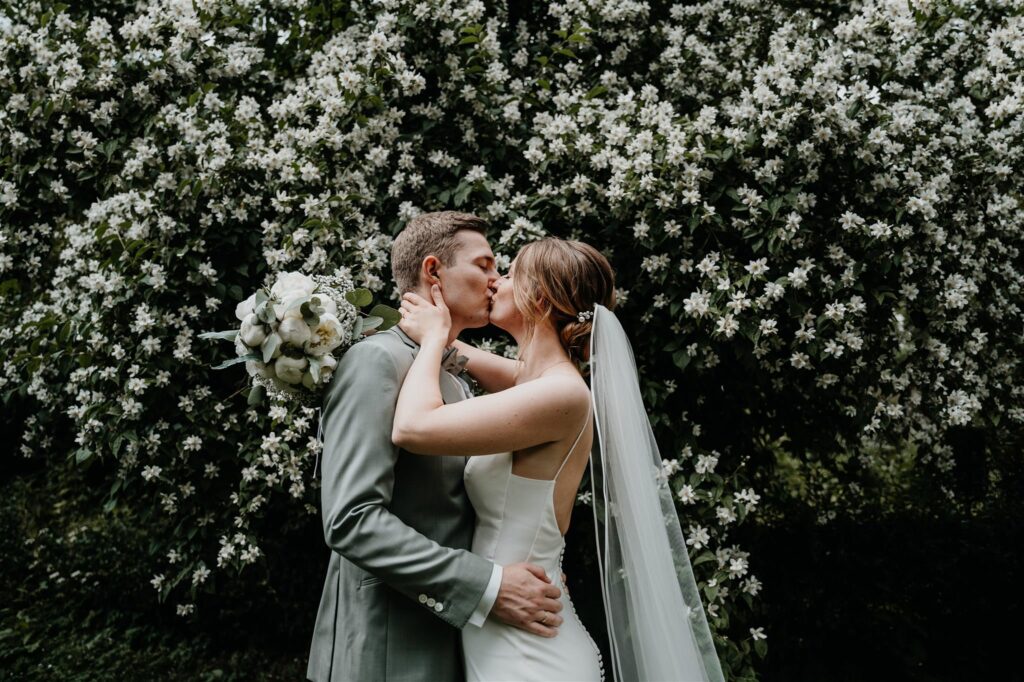 Küssendes Hochzeitspaar vor Blumen auf Gut Panker